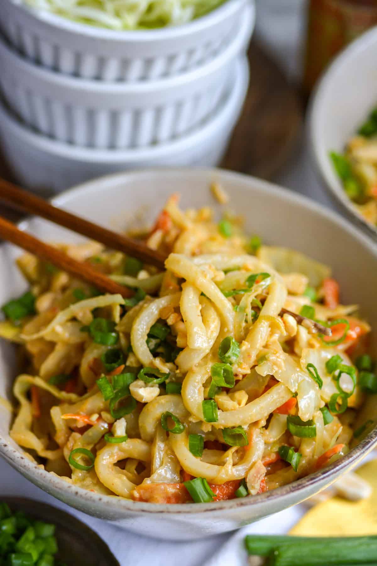Chopsticks holding a bite of Vegan Spicy Peanut Udon Noodles.