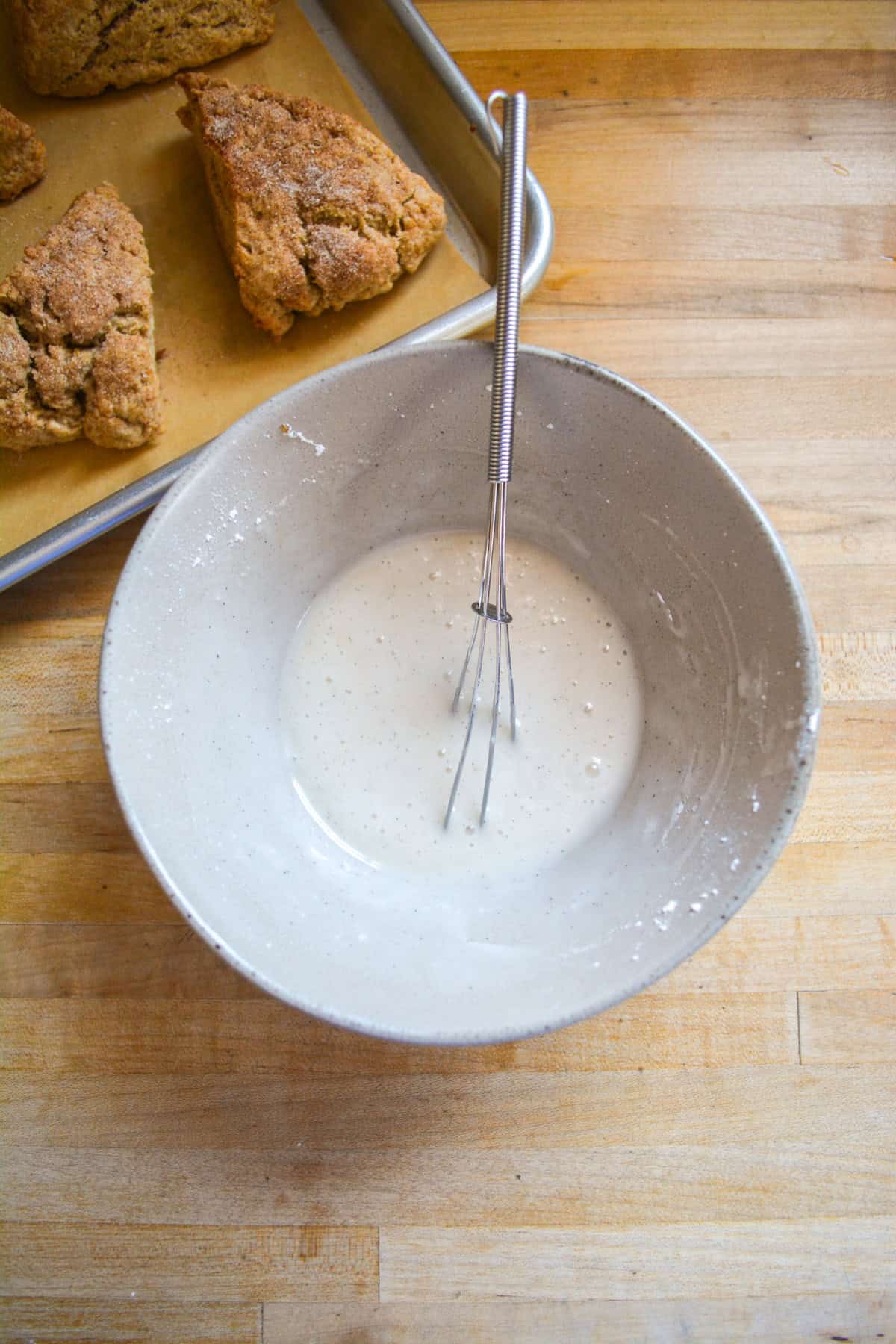 Bakes scones on a pan and vanilla glaze in a small bowl with a whisk.