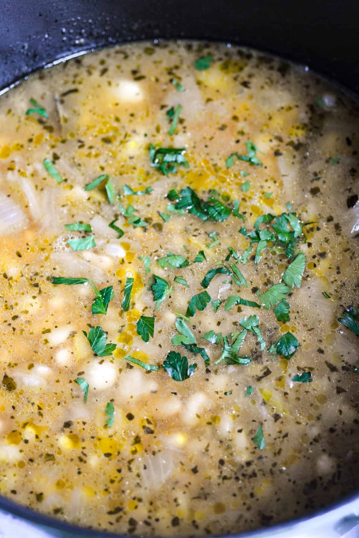 Cooked Brothy Great Northern Beans in a large pot topped with parsley.