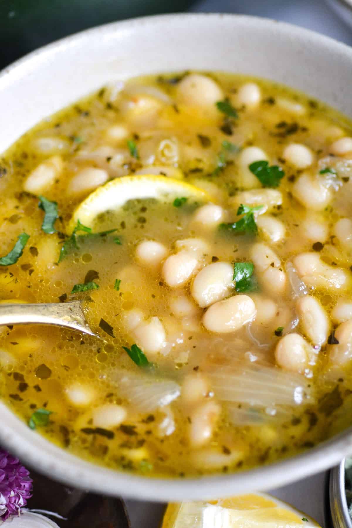Brothy Great Northern Beans in a bowl with a gold spoon.