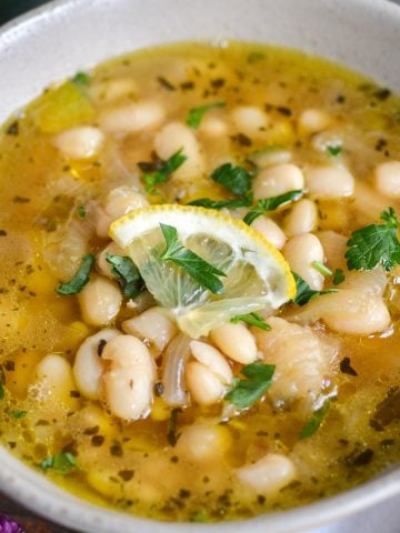 Brothy Great Northern Beans in a bowl topped with a slice of lemon.