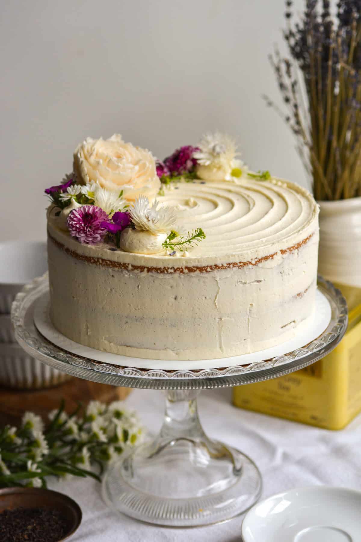 Earl Grey Lavender Cake topped with flowers on a glass cake stand.