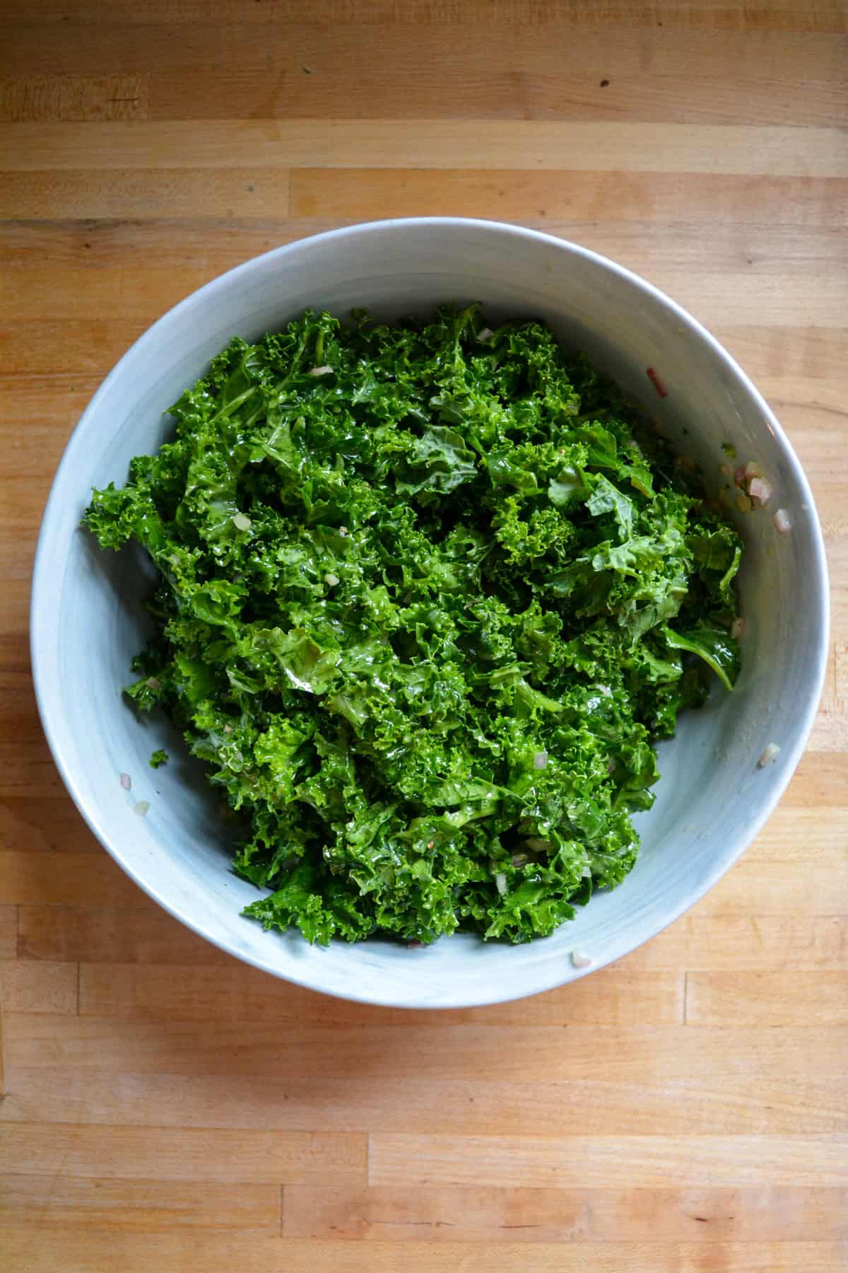 Kale massaged with the salad dressing in a large bowl.