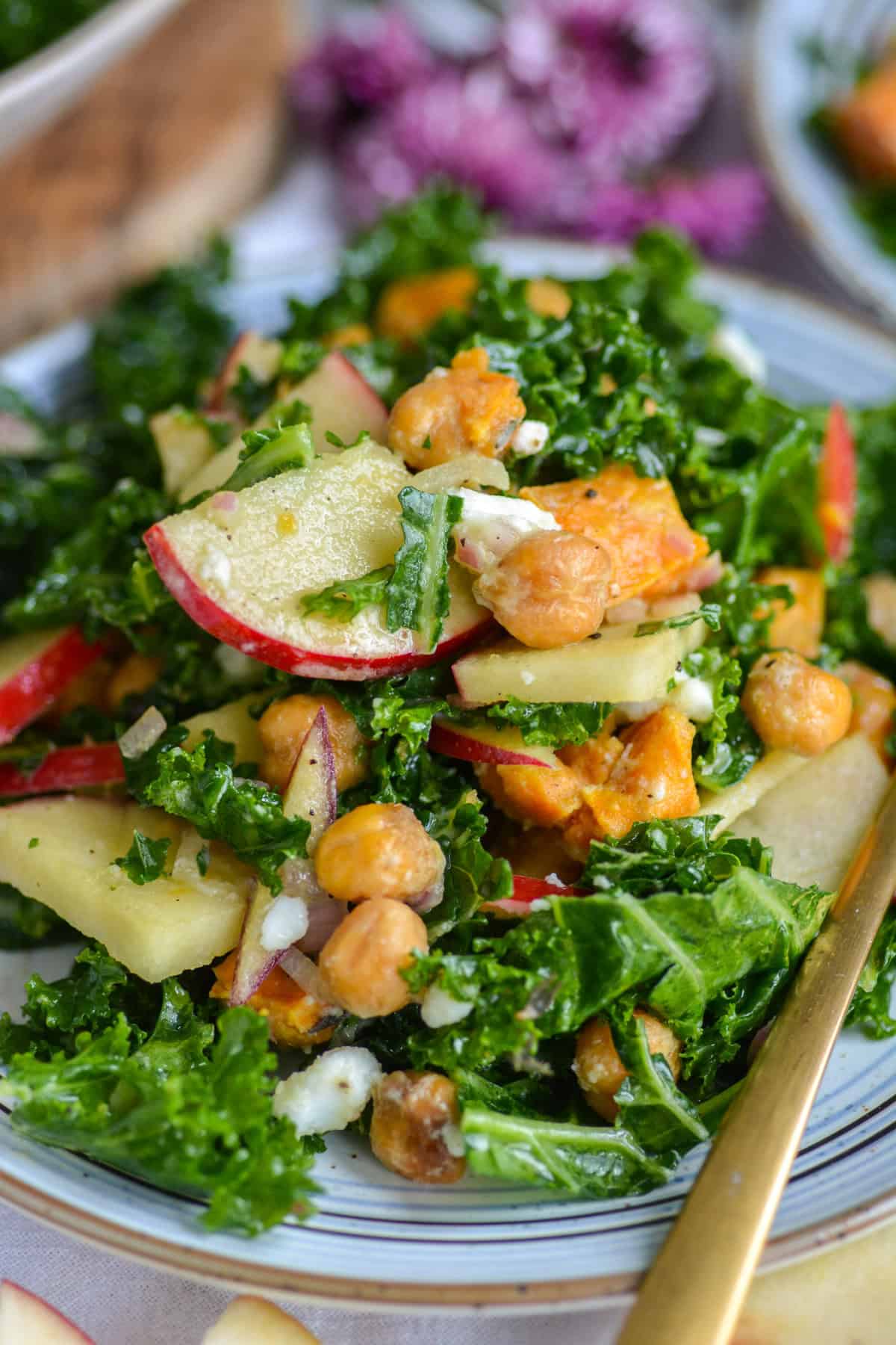 Kale Sweet Potato Salad topped with sliced apple on a plate with a gold fork.