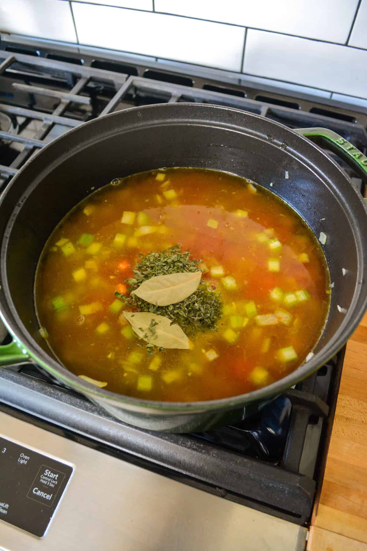 Herbs added into soup cooking in a Dutch oven.