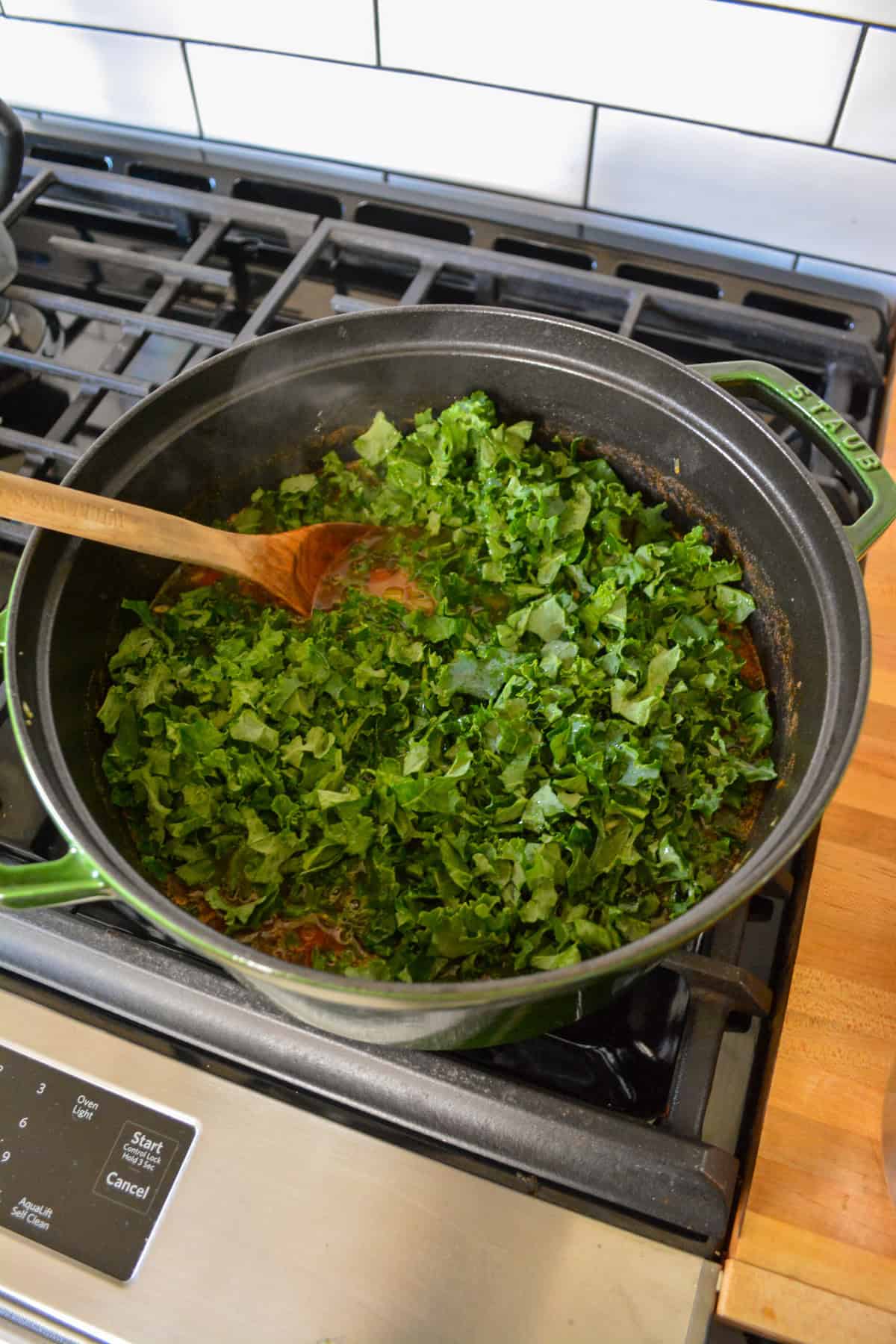 Kale added into Tuscan White Bean Soup in a large pot.