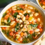 Vegan Tuscan White Bean Soup in a bowl with a gold spoon.