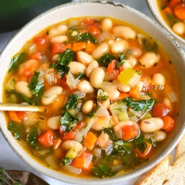 Vegan Tuscan White Bean Soup in a bowl with a gold spoon.