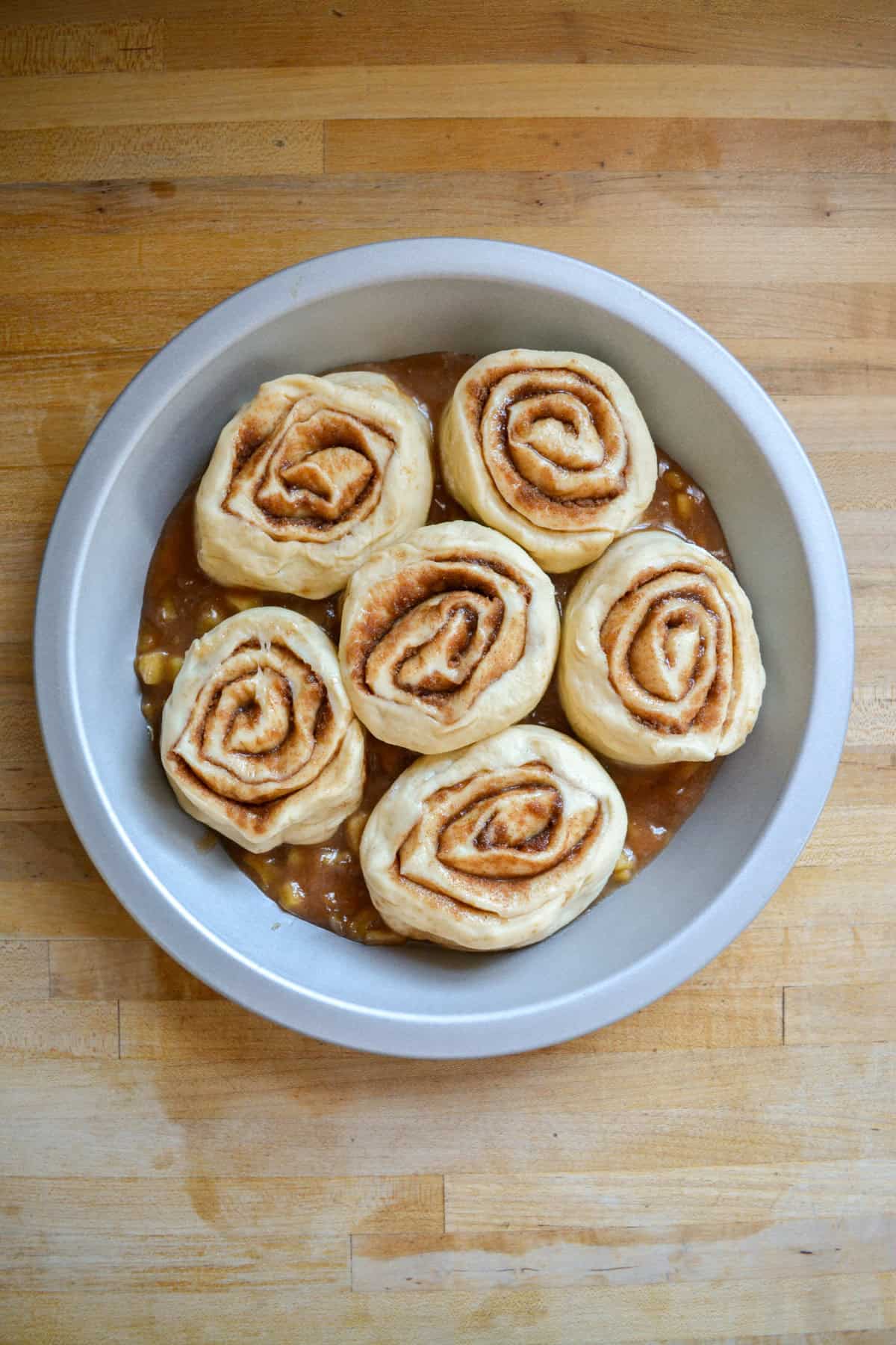 Cinnamon rolls on top of apple pie filling in a deep dish pie plate.