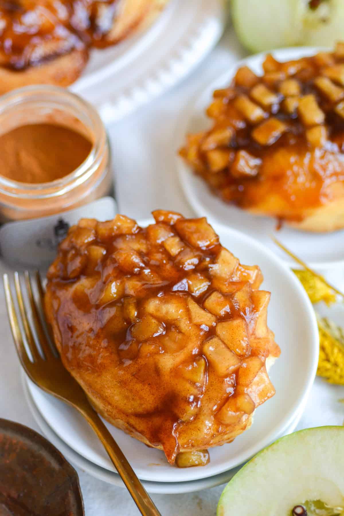 Apple Pie Cinnamon Roll on a plate with a gold fork.