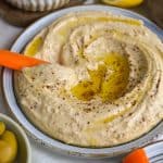 A carrot stick dipped into Red Lentil Hummus on a plate.