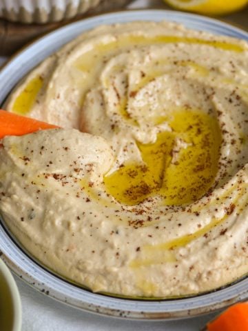 A carrot stick dipped into Red Lentil Hummus on a plate.