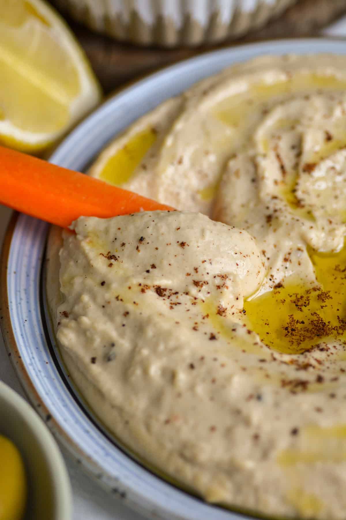 A carrot dipped into a plate of red lentil hummus.