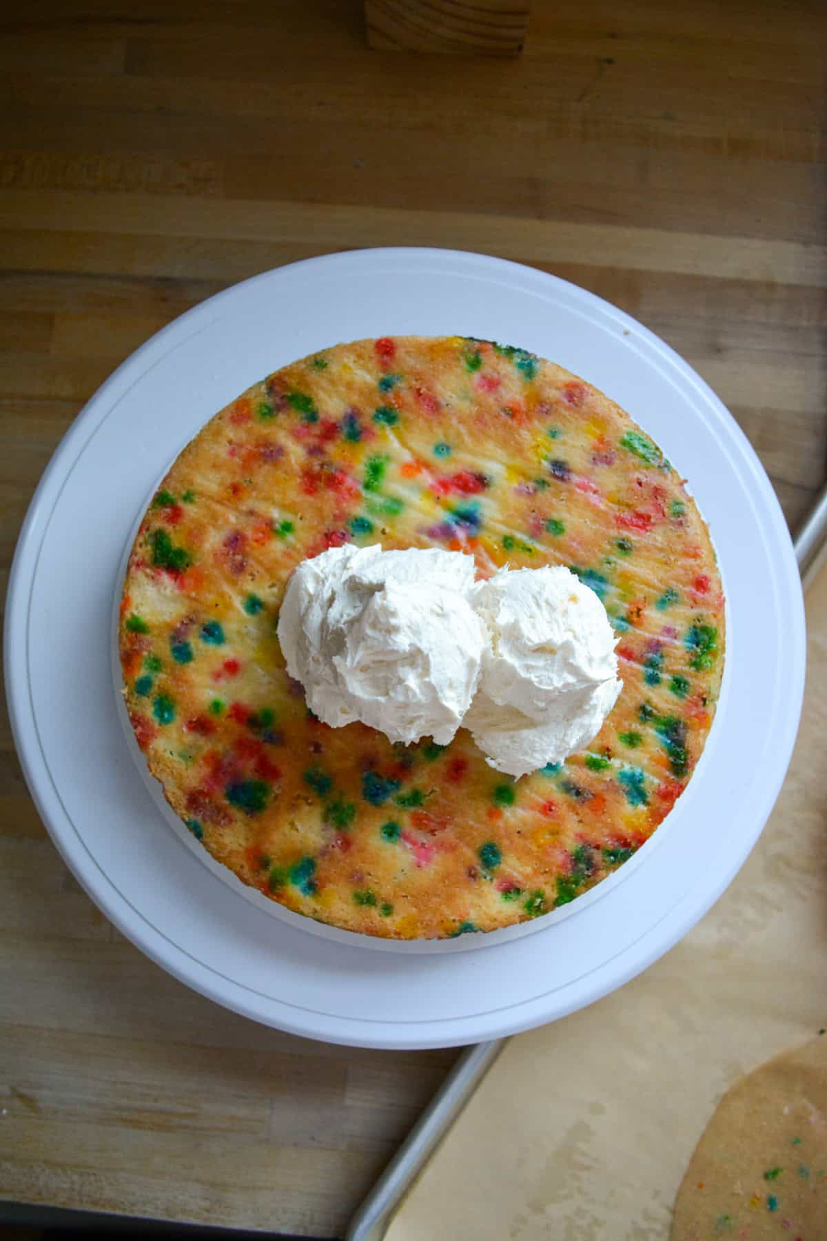 A cake layer on a cake stand with frosting scooped on top of it.