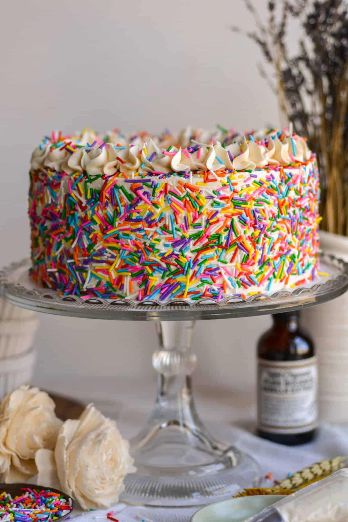 A Vegan Funfetti Cake covered in sprinkles on a cake stand.
