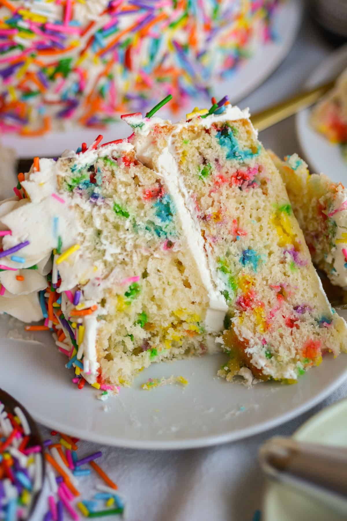 A bite taken out of a piece of Vegan Funfetti Cake on a white plate.