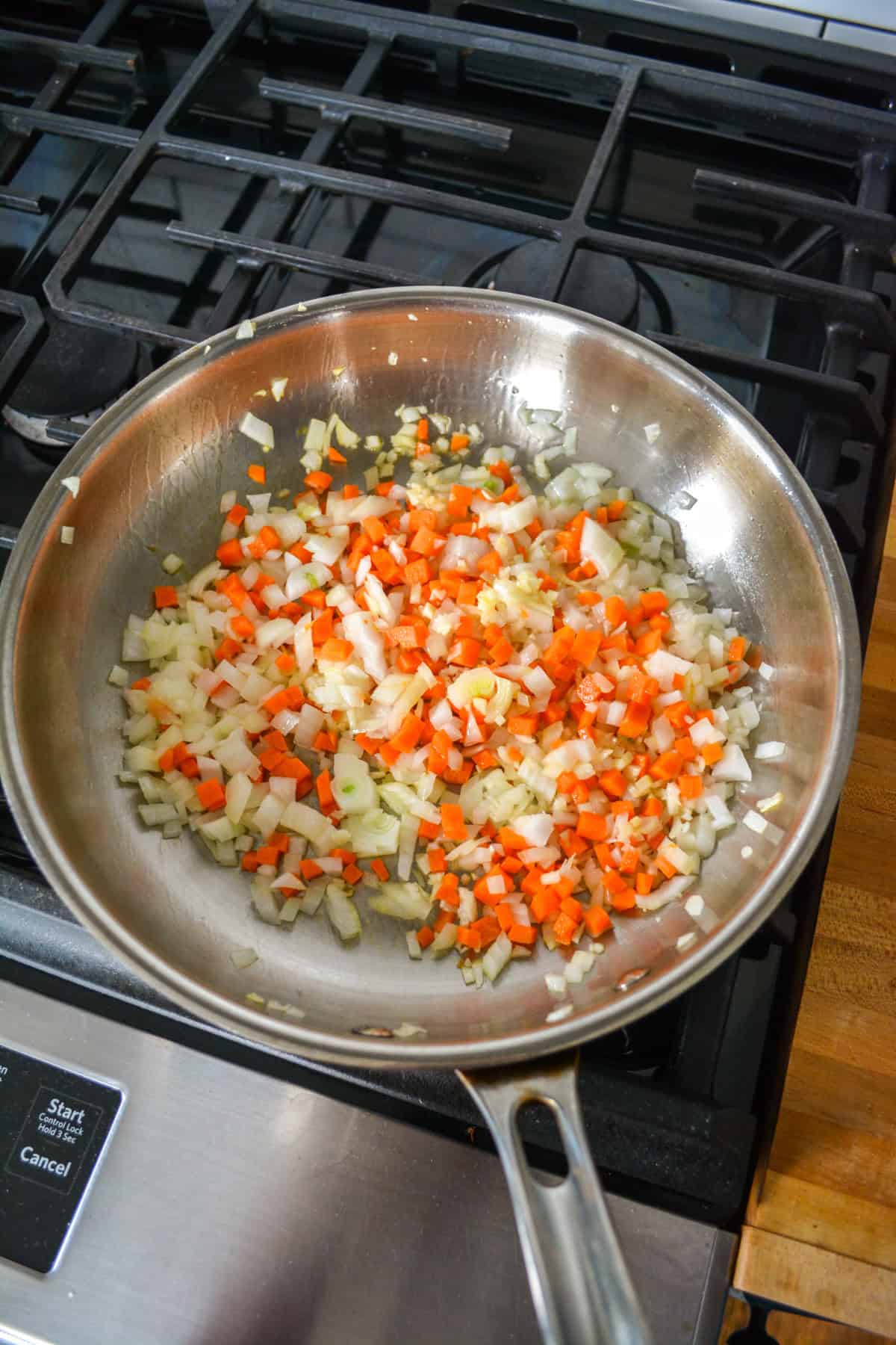 Chopped carrots and onion cooking in a stainless-steel skillet.