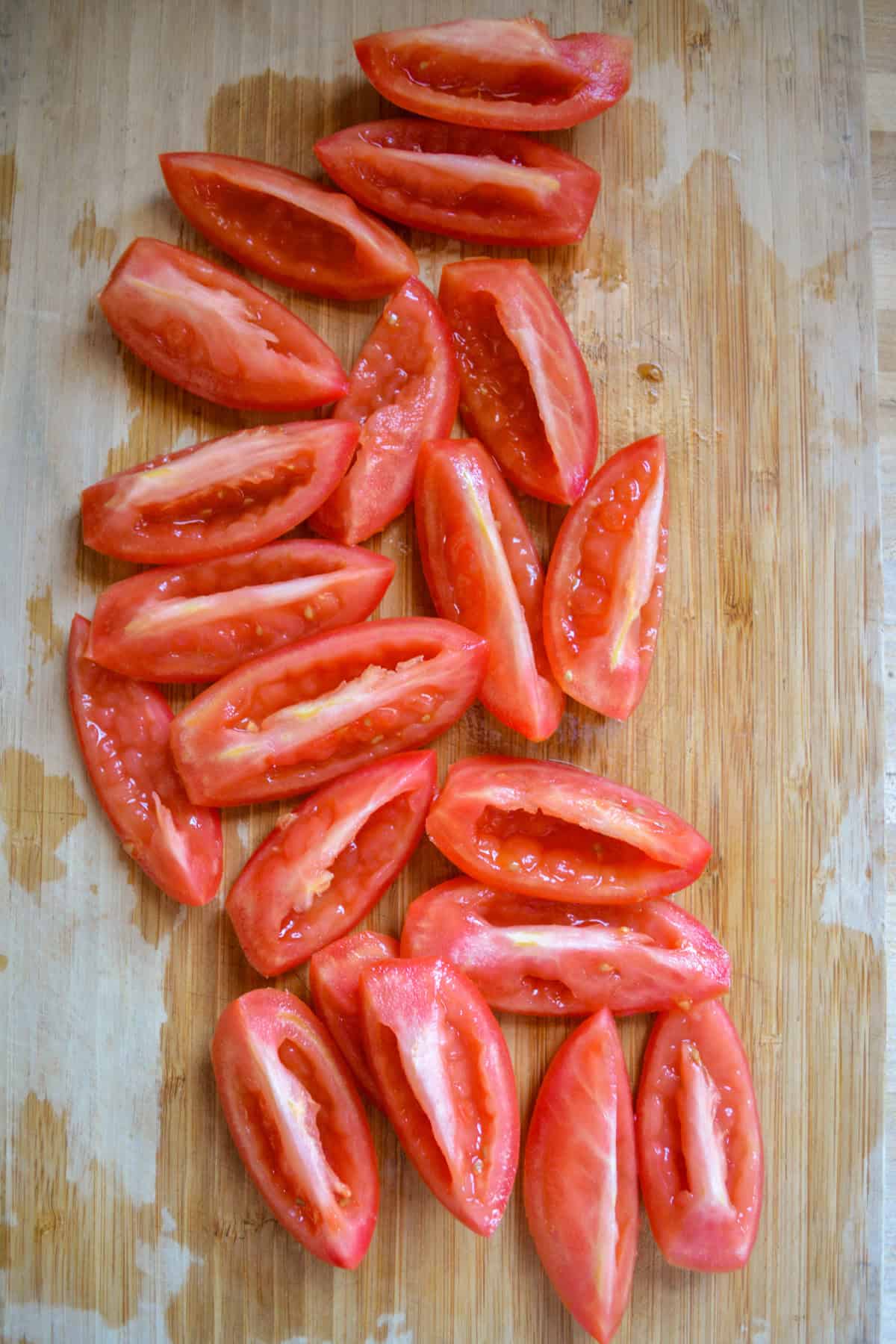 Quartered and seeded tomatoes on a wooden cutting board.