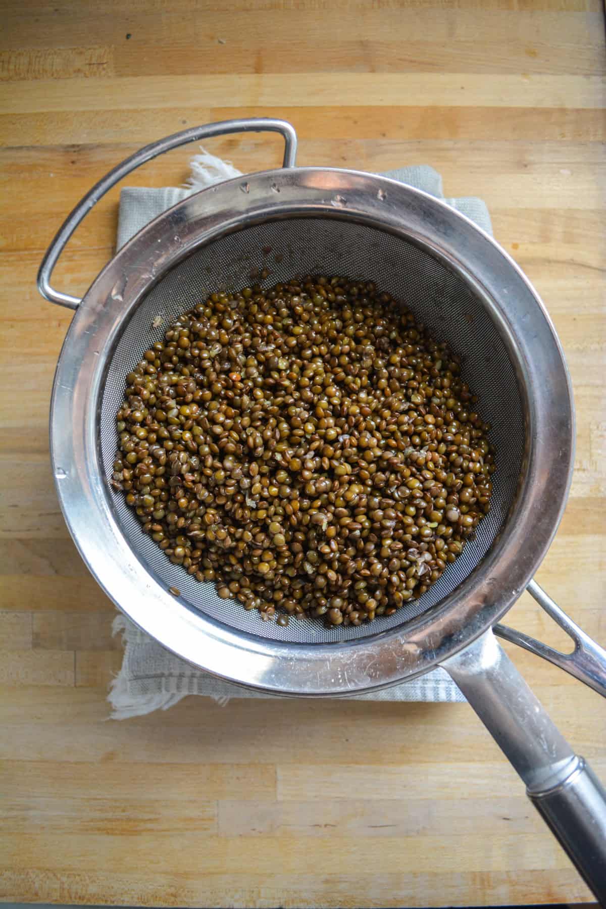 Cooked black lentils in a fine mesh strainer.