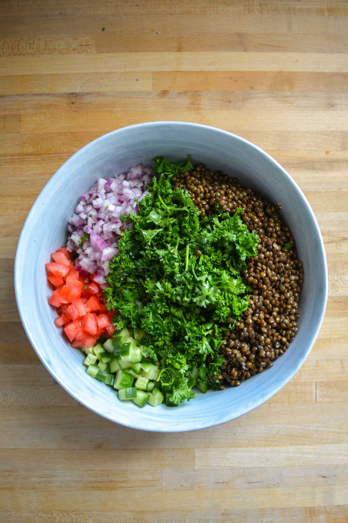 Lentils, parsley, onion, tomato and cucumber in a large bowl.