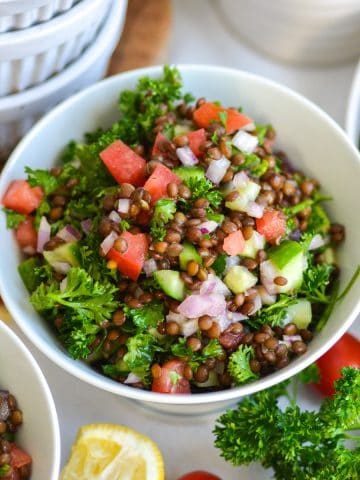 Mediterranean Black Lentil Salad in a bowl with chopped tomatoes, cucumber and parsley.