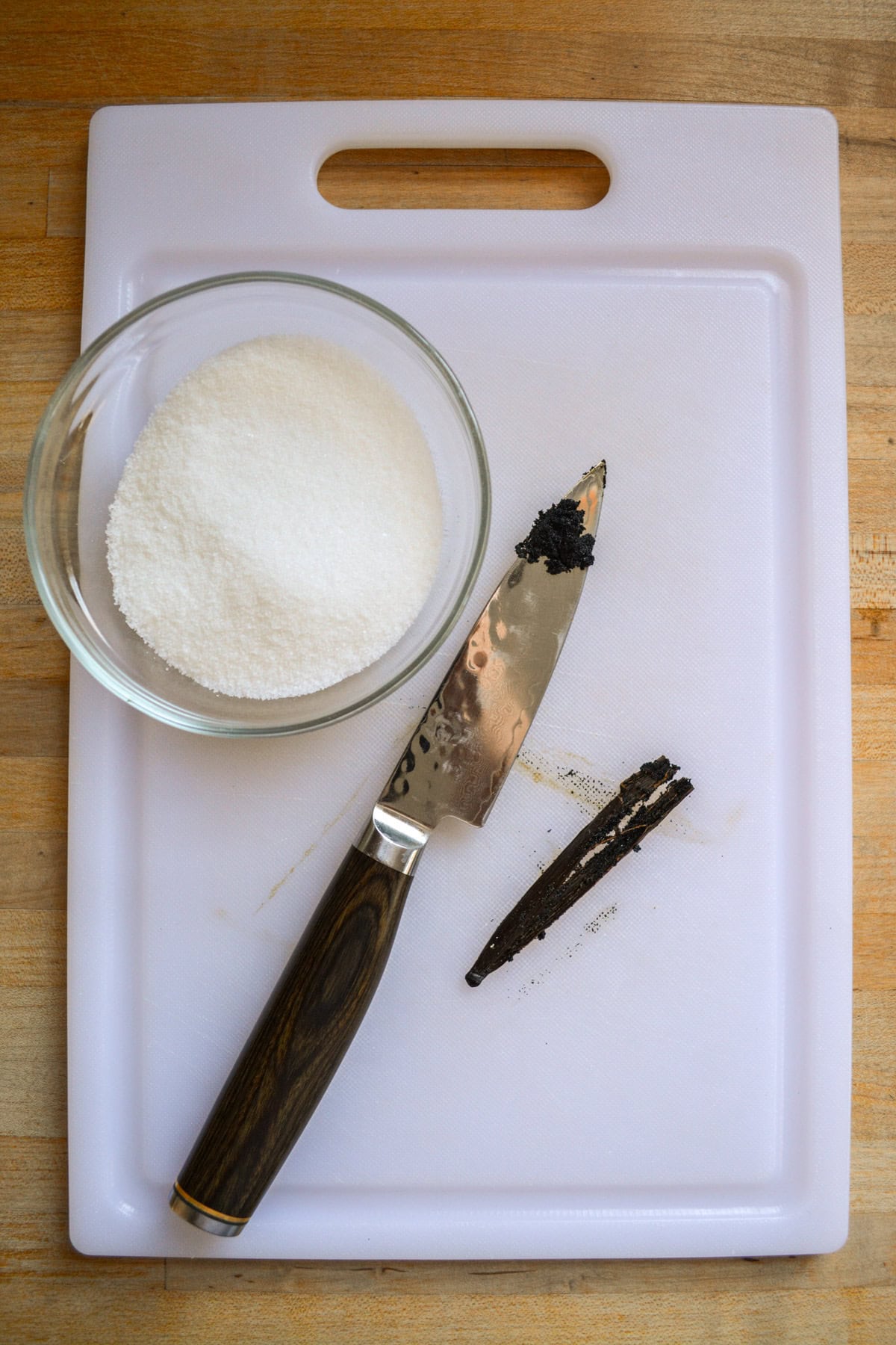 A paring knife with vanilla bean seeds on it next to a vanilla bean pod.