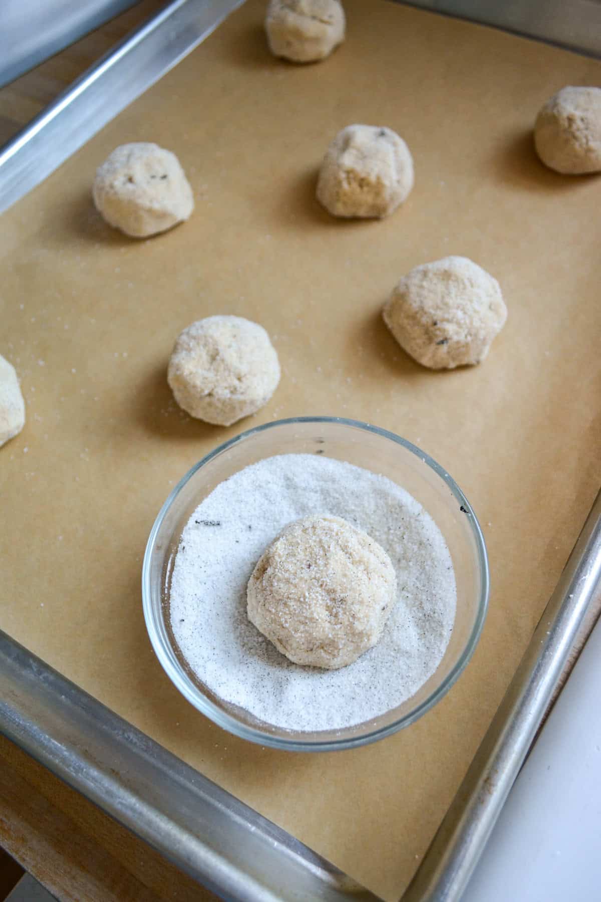 Rolling cookie dough balls in vanilla sugar and placing them on a baking sheet.