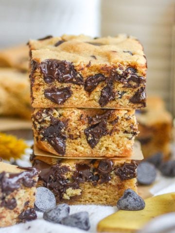 Three Vegan Blondies stacked on top of each other with chocolate chips scattered around.