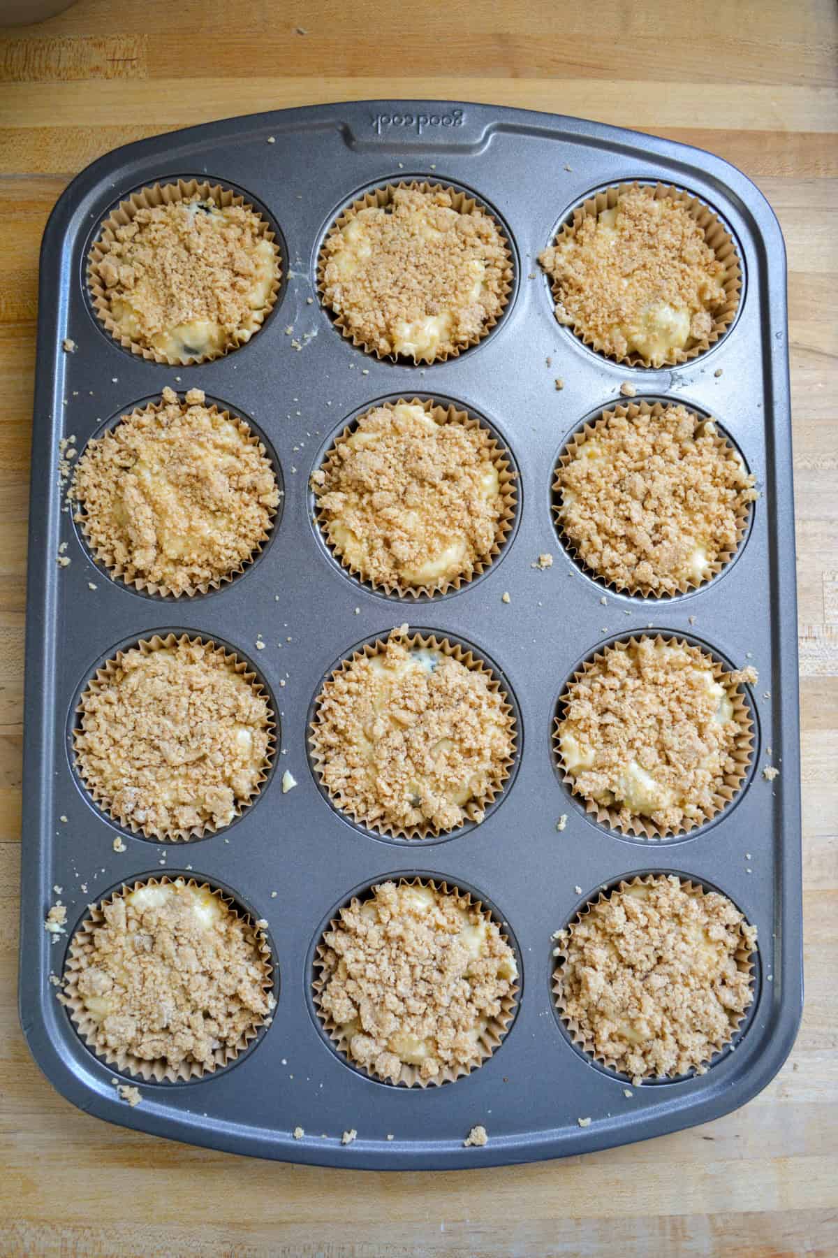 Vegan blueberry muffin batter in a muffin tin topped with streusel.