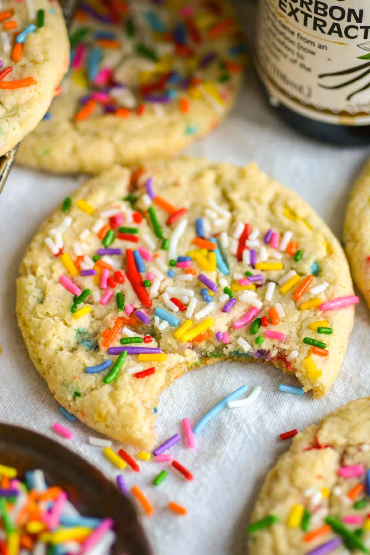 A bite taken out of a Vegan Funfetti Cookie with sprinkles on top on a linen cloth.