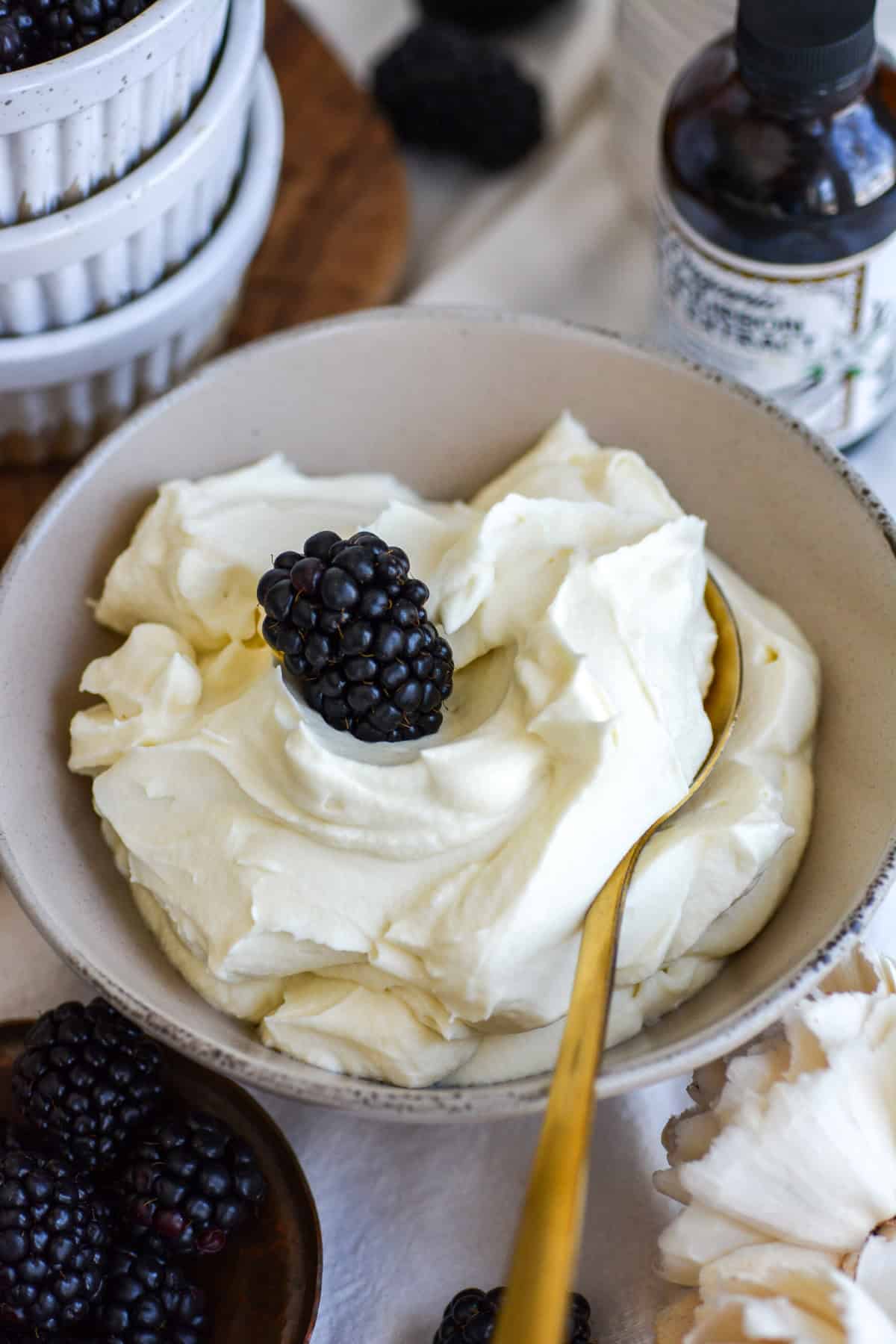 Vegan Whipped Cream Frosting in a bowl with a gold spoon and a blackberry.
