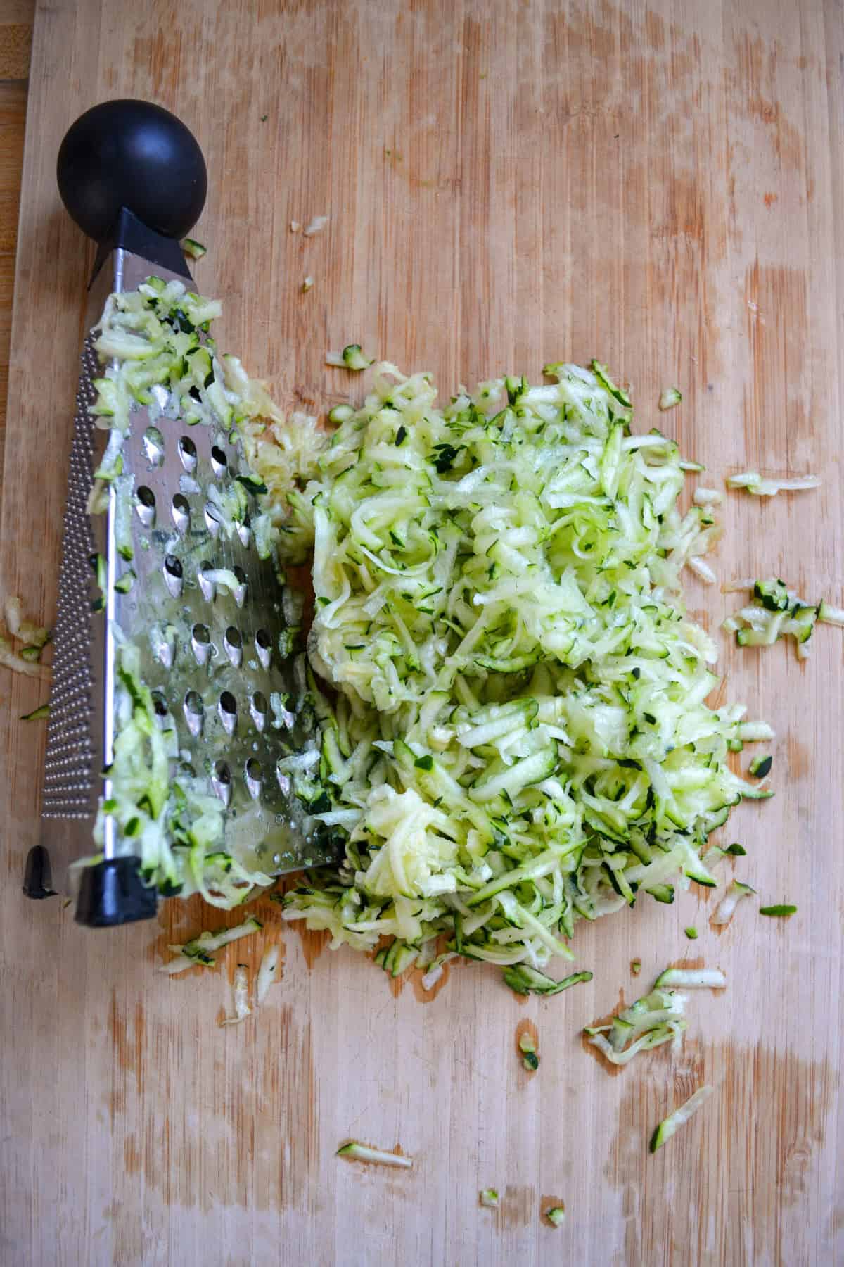Grated zucchini next to a box grater on a wooden cutting board.