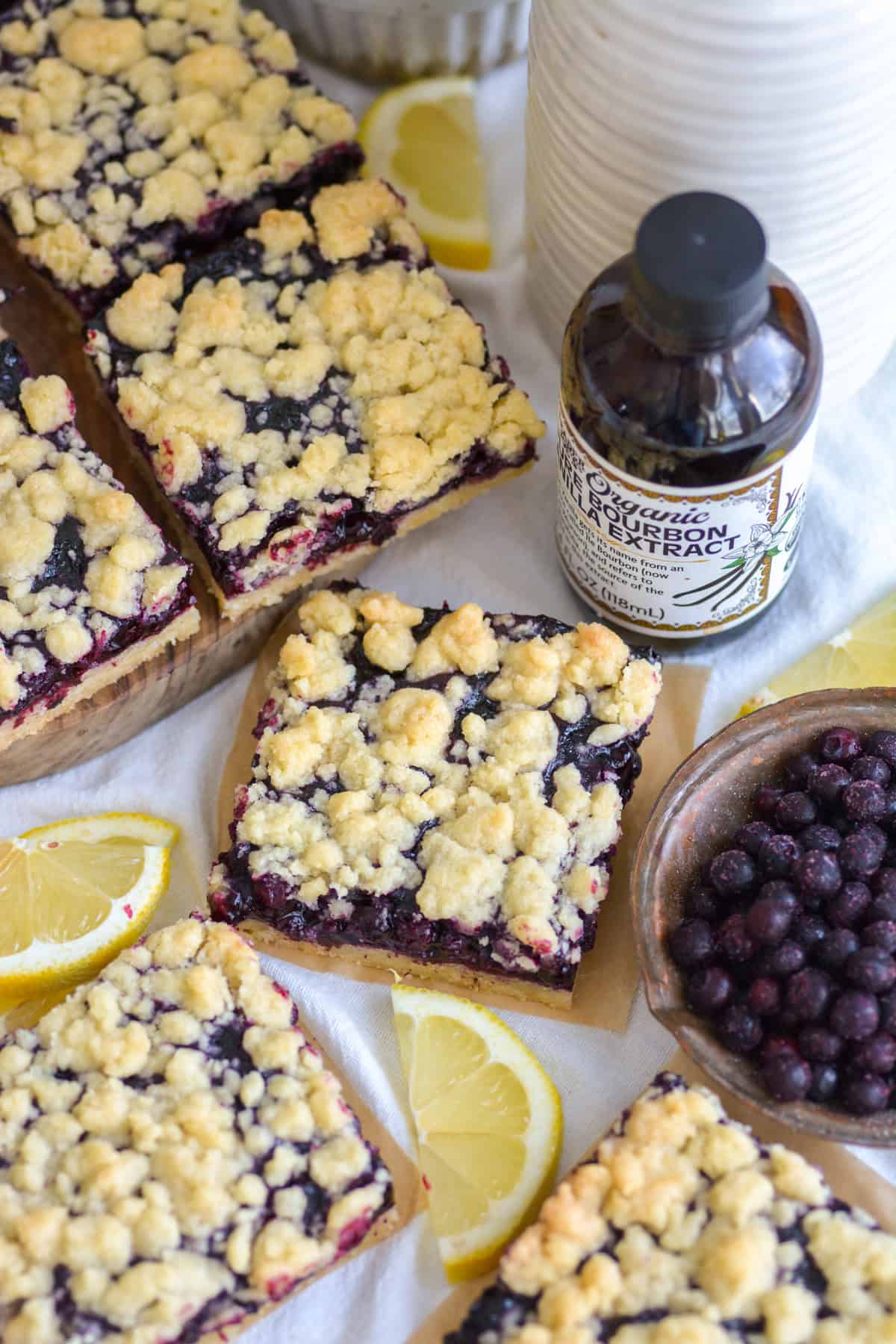 Blueberry Crumble Bars on a linen surface with slices on lemon in the scene.