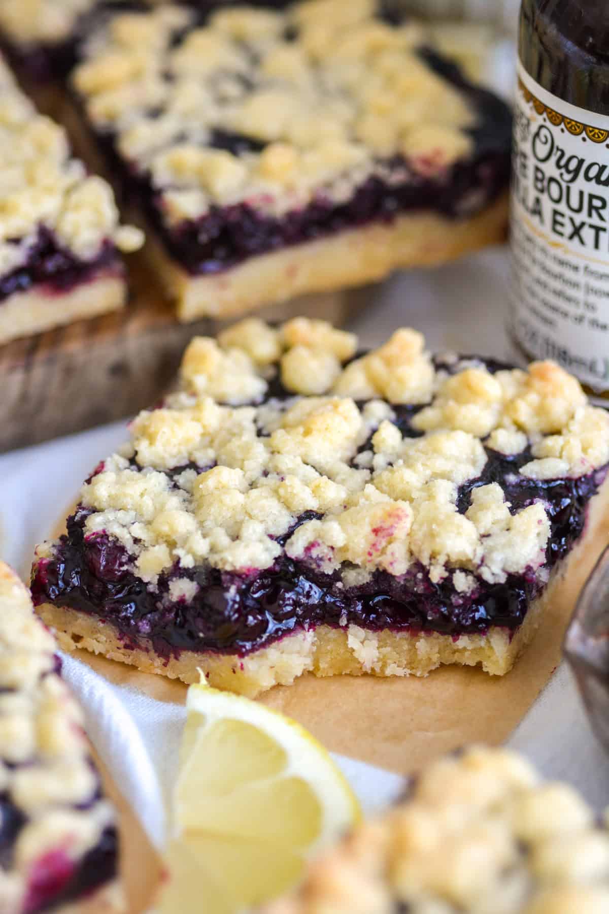 Blueberry crumble bar with a bite taken out of it on a piece of parchment paper.