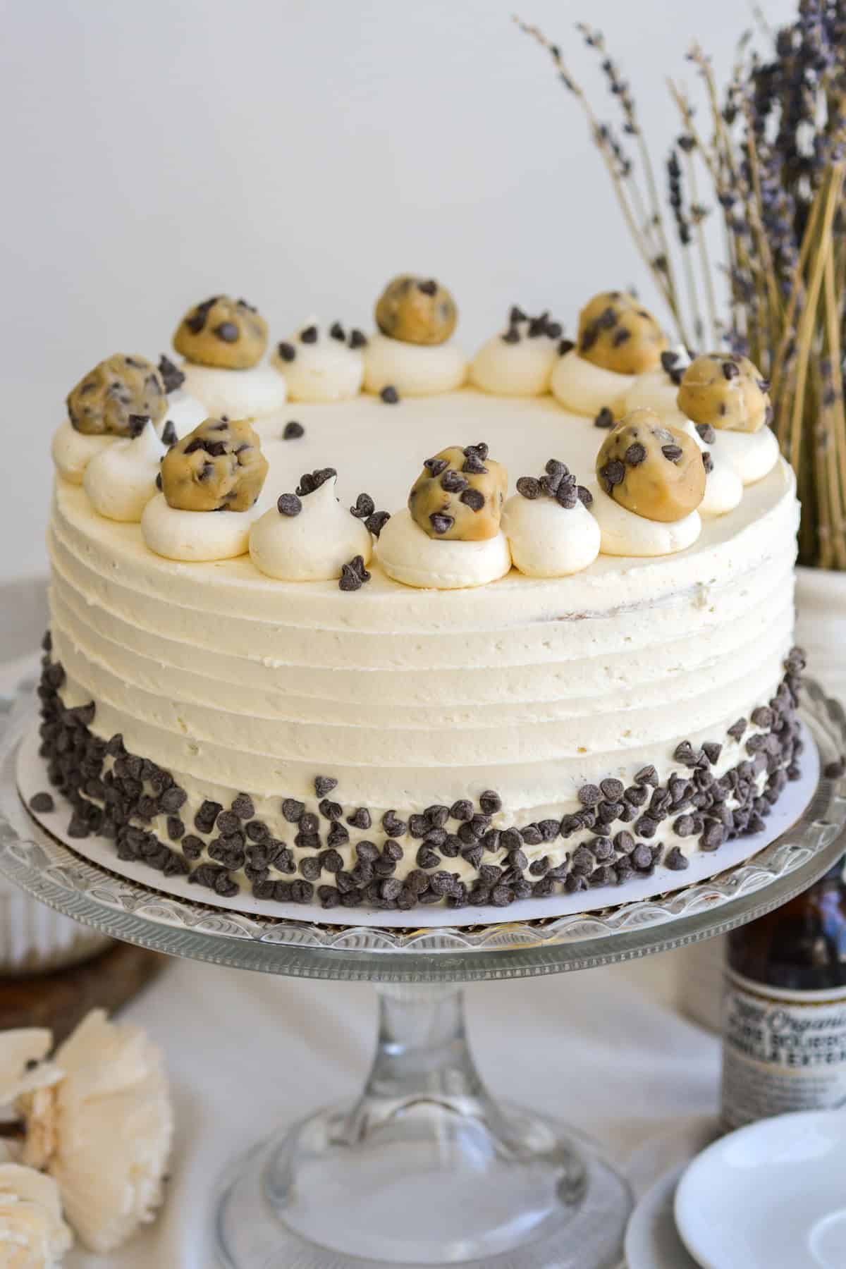 Cookie Dough Cake topped with chunks of cookie dough on a glass cake stand.