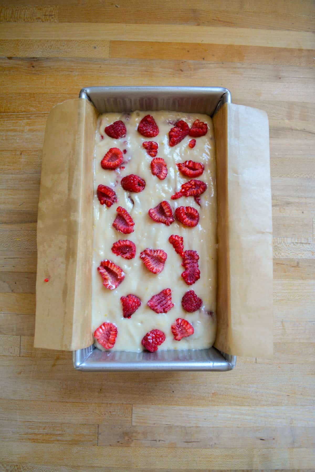 Cake batter in a loaf pan topped with fresh raspberries.