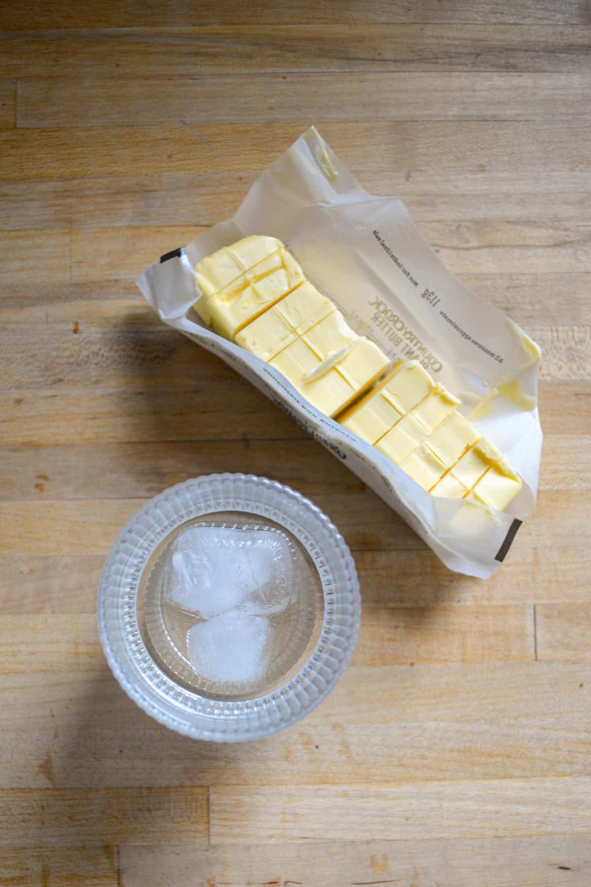 Cubed butter and a glass of ice water on a wooden surface.