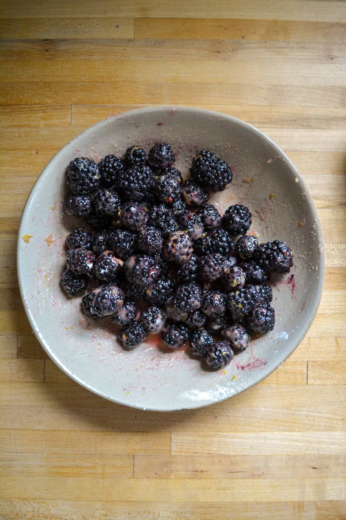 Fresh blackberries mixed with sugar and lemon juice in a bowl.