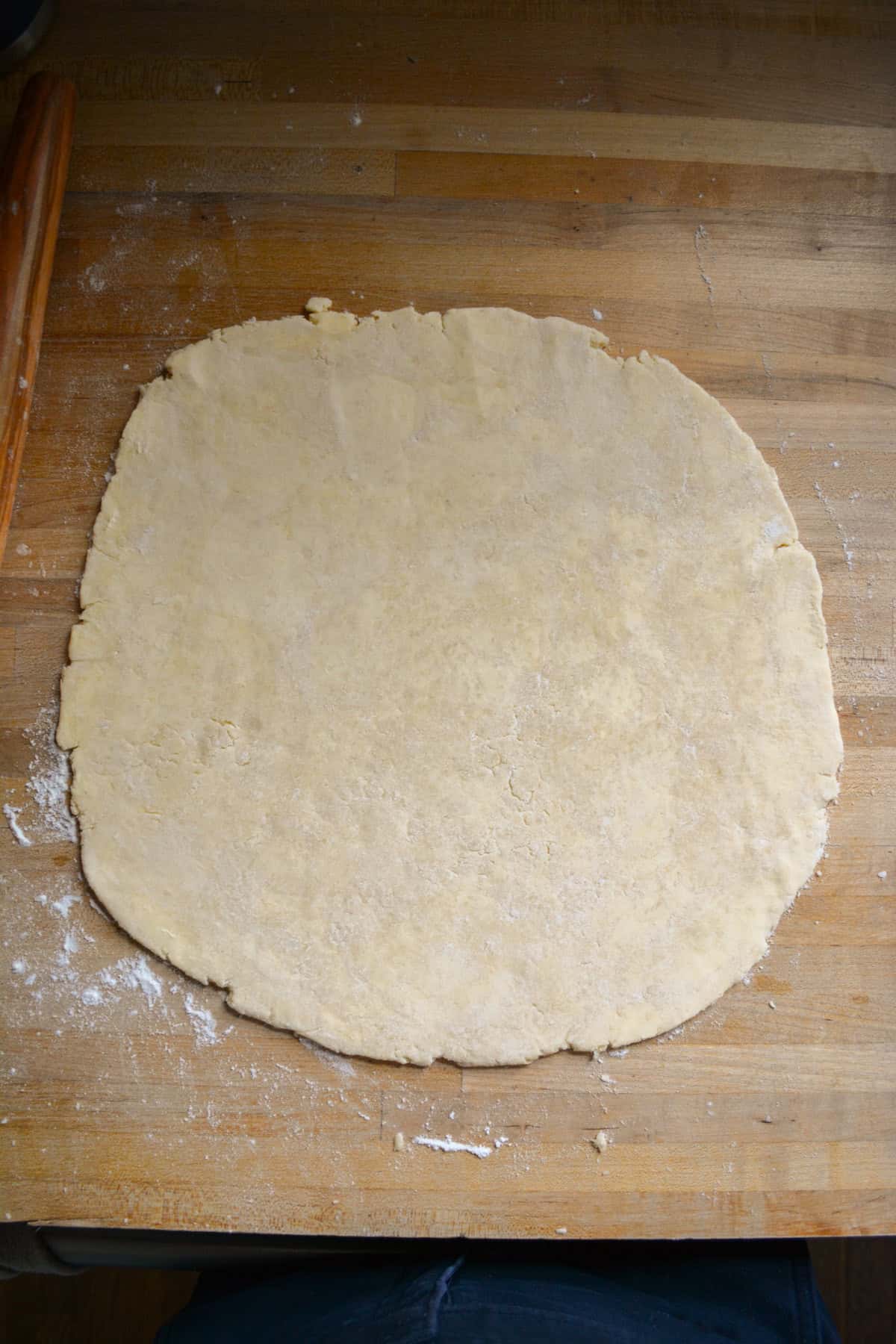 Pie dough rolled into a circle on a wooden surface.
