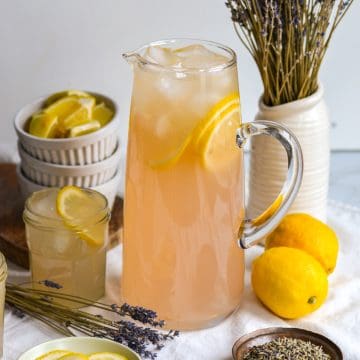 Lavender Lemonade in a pitcher with lemon slices and ice.