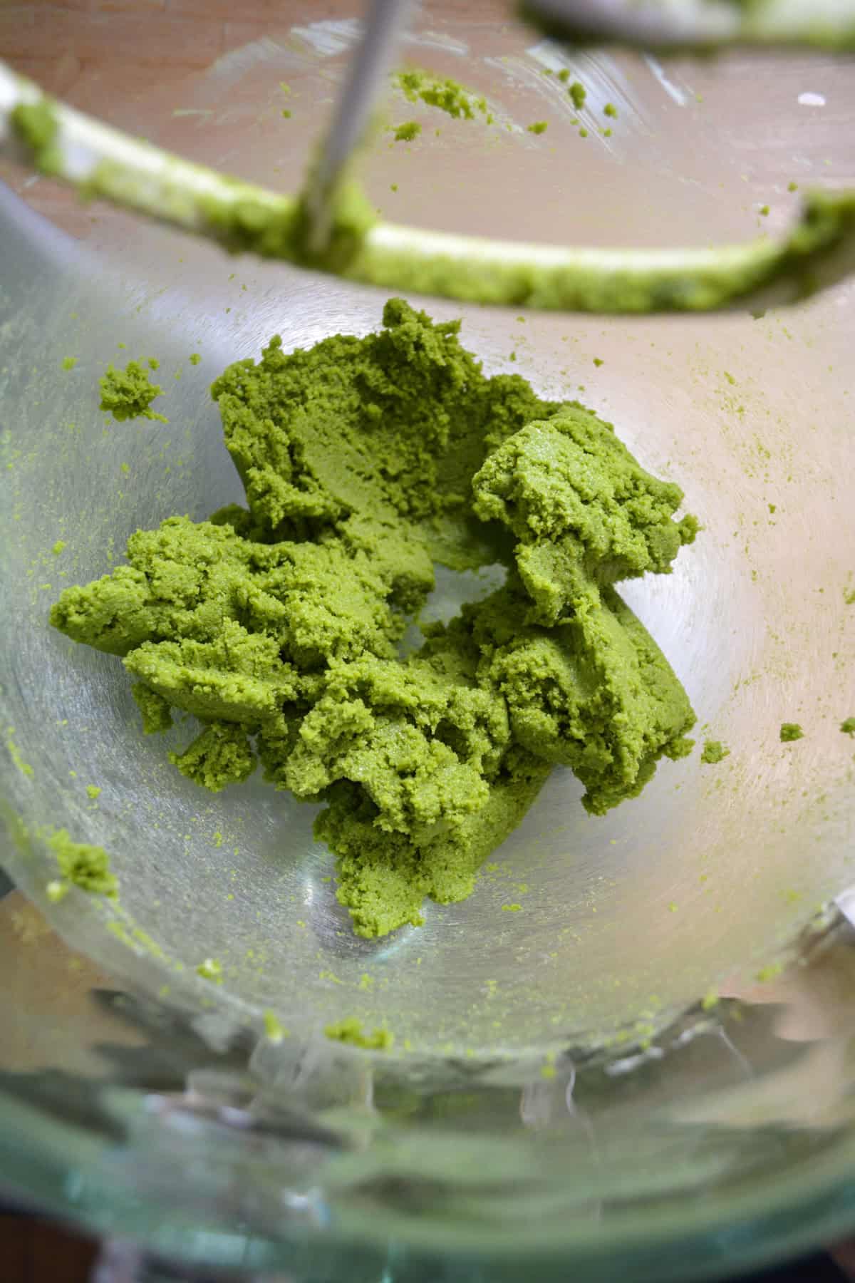 Butter, sugar and matcha powder creamed together in a glass mixing bowl.