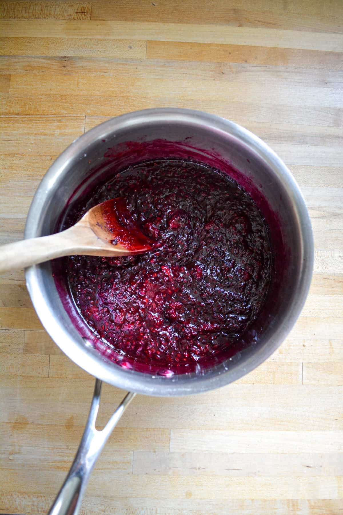 Simmered blackberry filling in a saucepan with a wooden spoon.