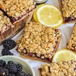 Blackberry Oat Bars on a linen surface with lemon slices and a small bowl of blackberries.