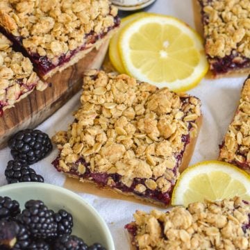 Blackberry Oat Bars on a linen surface with lemon slices and a small bowl of blackberries.