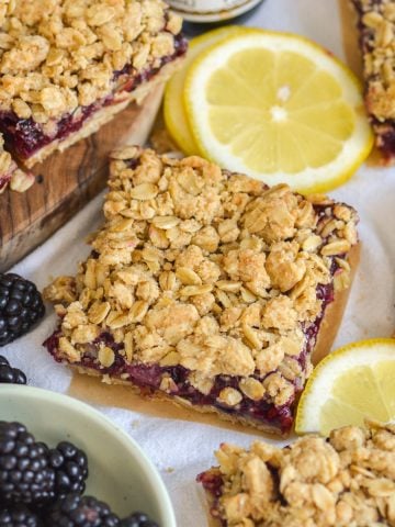 Blackberry Oat Bars on a linen surface with lemon slices and a small bowl of blackberries.