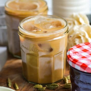 A Cardamom Latte in a glass on a wooden board.