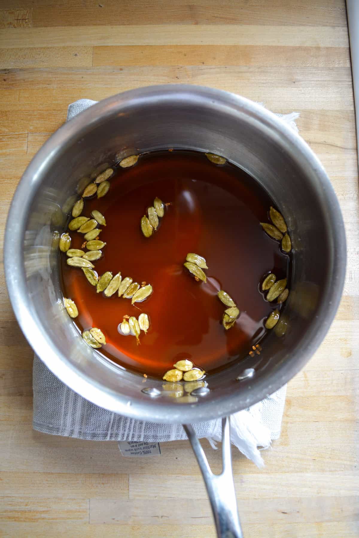 Cardamom syrup in a pot with cardamom pods.