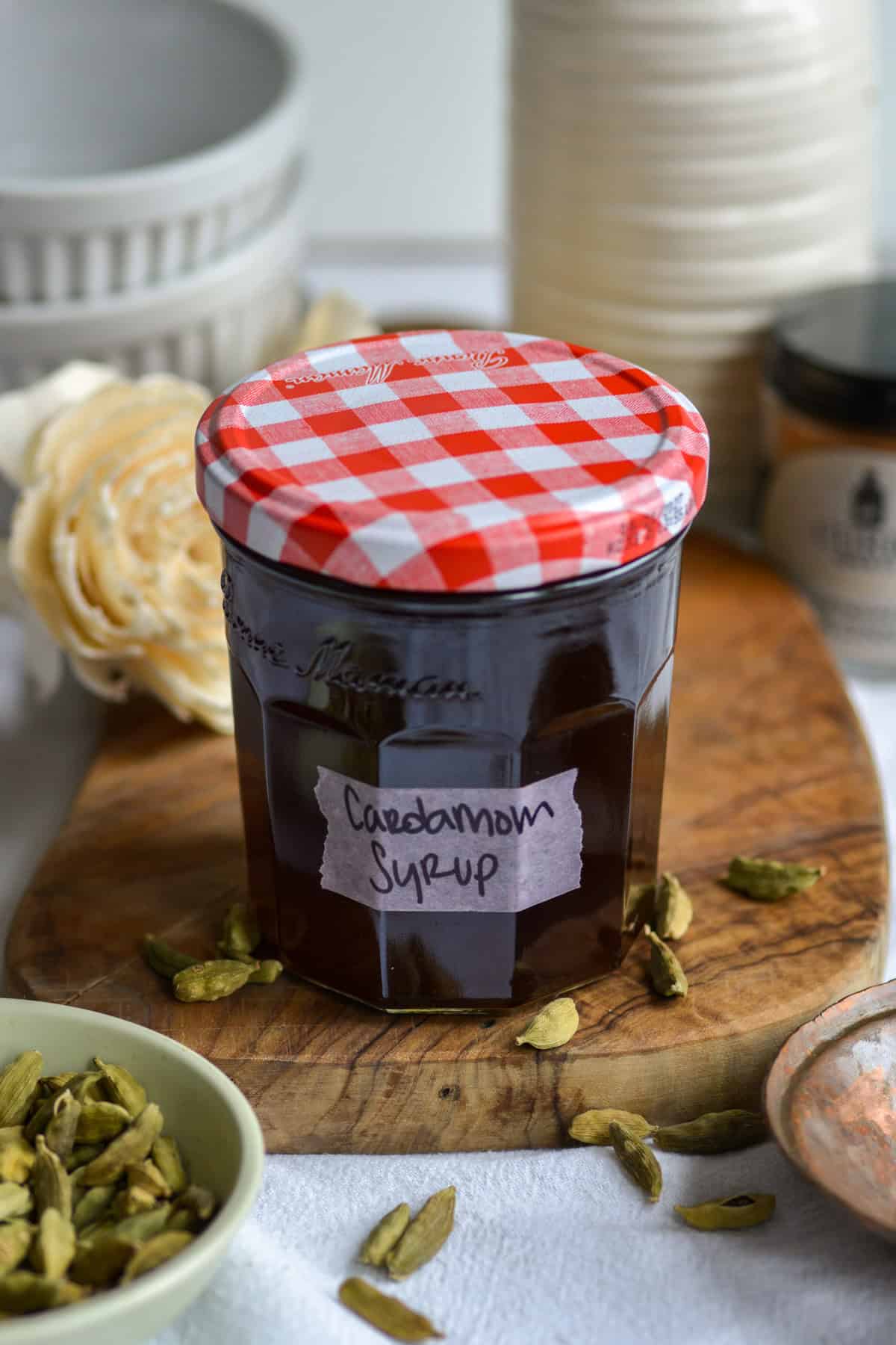 Cardamom syrup in a glass jar on a wooden board.