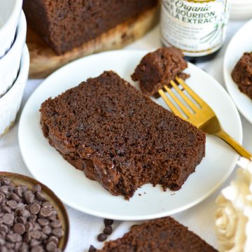 A slice of Chocolate Chocolate Chip Loaf Cake on a small plate with a bite taken out of it.
