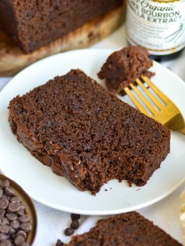 A slice of Chocolate Chocolate Chip Loaf Cake on a small plate with a bite taken out of it.